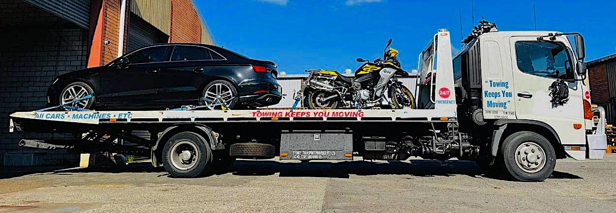 A car and motorbike on the back of a tilt tray tow truck.