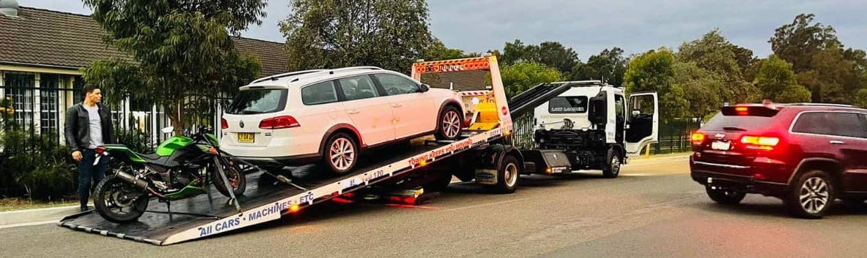 A car and a motorcycle getting towed by a tilt tray truck.