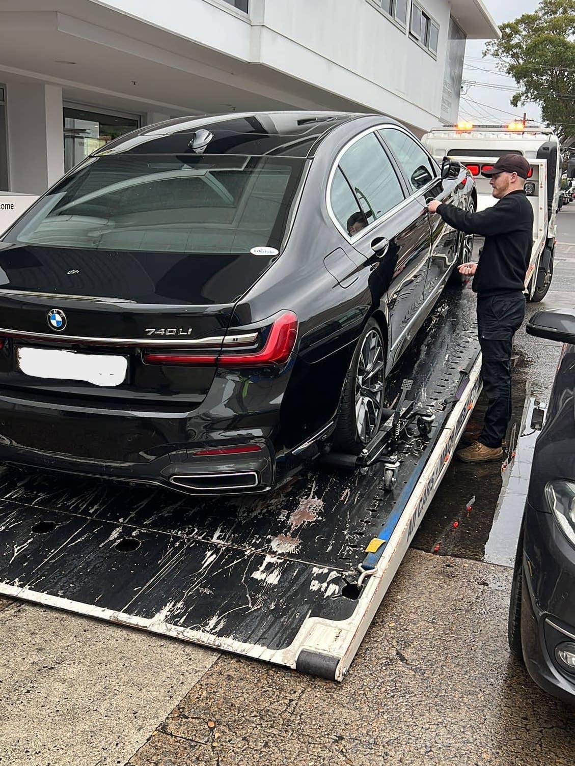 A BMW getting transported by a tilt tray tow truck.