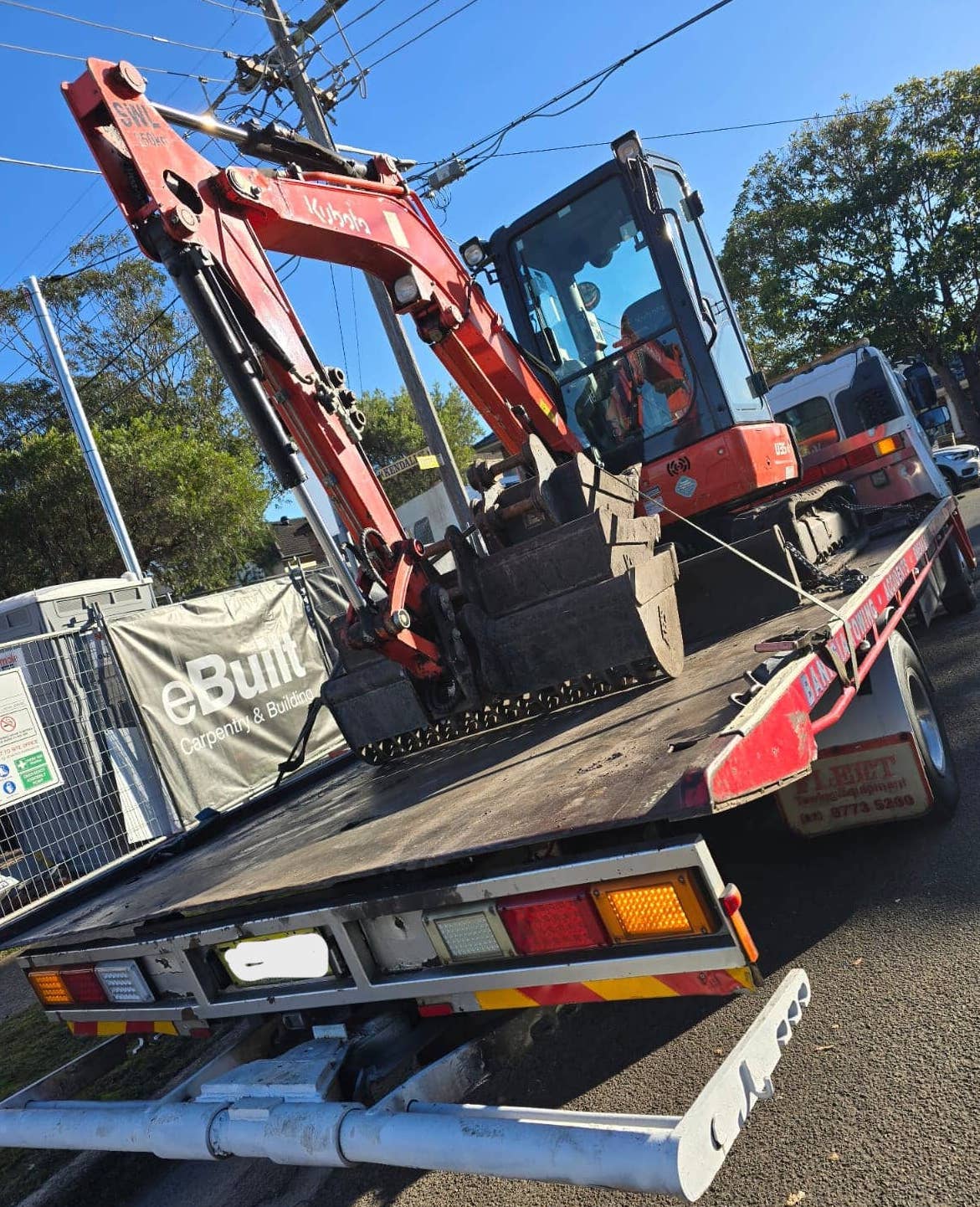 An excavator getting towed by a tilt tray truck.