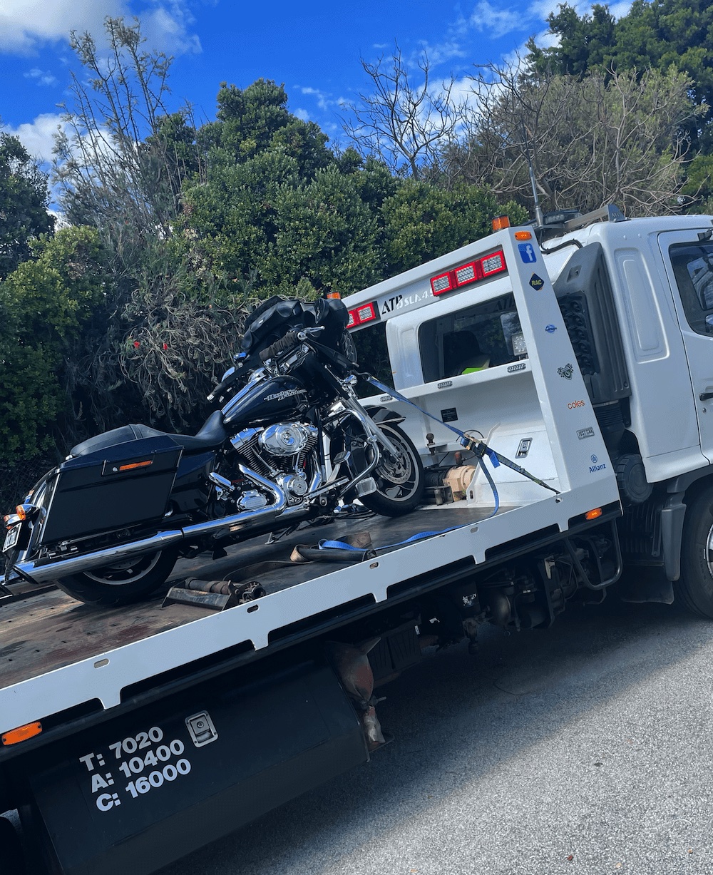 Tilt tray tow truck transporting a black touring motorcycle.